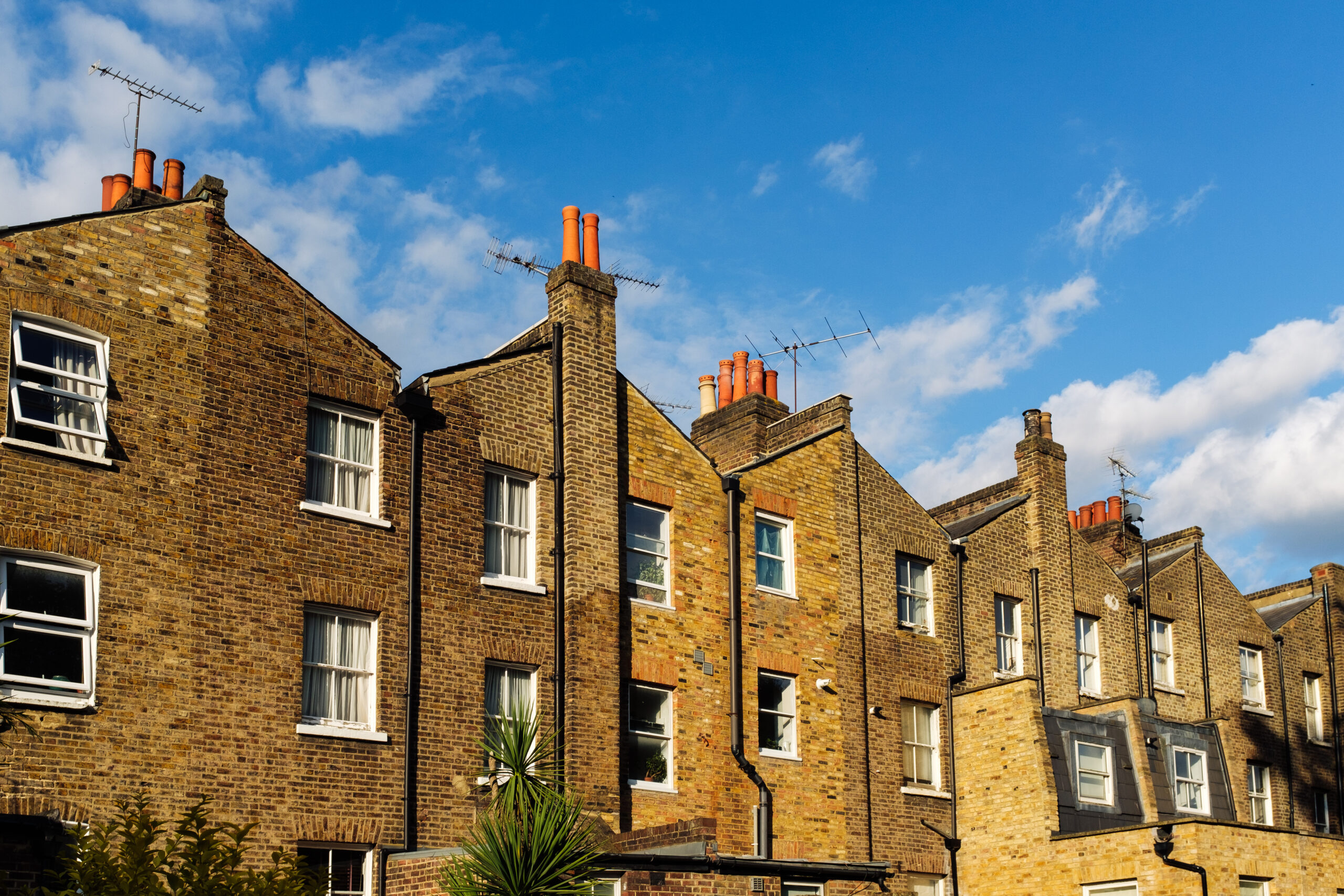 Terraced brick houses with chimneys and antennas under blue sky in london